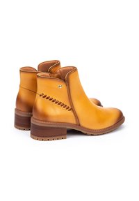 Botas de cuero hasta el tobillo en amarillo mostaza, con punta redonda, costuras texturizadas en los laterales y un tacón bajo apilado marrón.