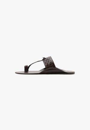 Sandale plate en cuir noir avec une large sangle tressée et une boucle pour l'orteil, vue de côté sur fond blanc.
