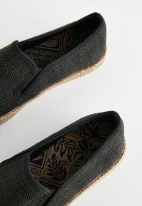 Zwarte stoffen instappers met een espadrille-achtige jute zool. Ingewikkelde geweven textuur en gestreepte binnenvoering in donkere tinten.
