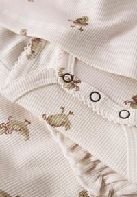 Abbigliamento per neonati in morbido beige a coste con anatroccoli marroni stampati e bottoni a pressione lungo il bordo arricciato dell'apertura del capo.