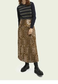 Jersey de rayas marineras con hilos metálicos, combinado con una falda plisada de color oro metálico con patrones florales. Botas negras gruesas completan el conjunto.