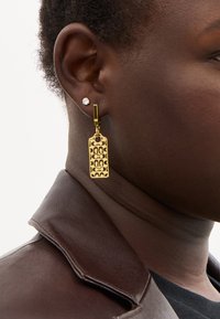 Guldörhängen i hängande modell med en rektangulär form och ett mönstrat ytskikt. Satta på en guldtonad krok för säker bärning.