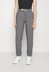 Juoda ir balta dryžuota jogger tipo kelnių su elastinga juosta, raišteliu ir uždarytomis kulkšnimis. Ant kairiojo klubo yra maža logotipo etiketė.