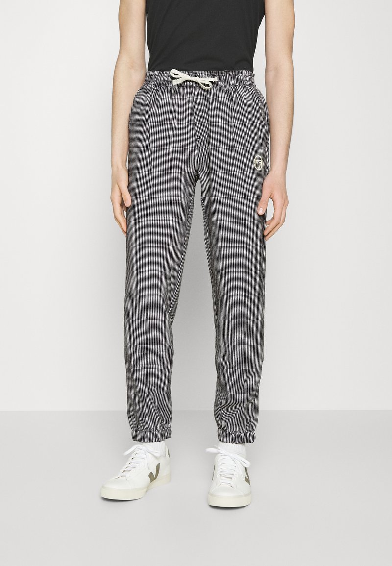 Juoda ir balta dryžuota jogger tipo kelnių su elastinga juosta, raišteliu ir uždarytomis kulkšnimis. Ant kairiojo klubo yra maža logotipo etiketė.