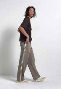 Bruine t-shirt met korte mouwen gecombineerd met beige wijde broek met witte zijkanten en crèmekleurige sneakers met textuuraccenten.