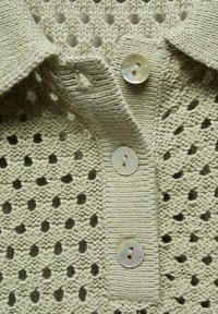 Polo lavorato a maglia verde chiaro con un motivo a rete testurizzato, dotato di colletto pieghevole e tre bottoni rotondi iridescenti.