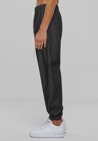 Dark gray jogger pants with elastic cuffs and waistband, featuring a white drawstring. Paired with white athletic sneakers.