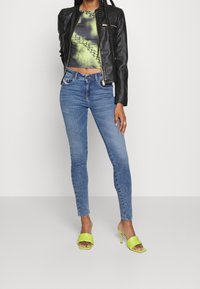 Svart läderjacka i kort modell, mångfärgad mönstrad toppen, ljusblå skinny jeans och limegröna klacksandaler med fyrkantig tå.