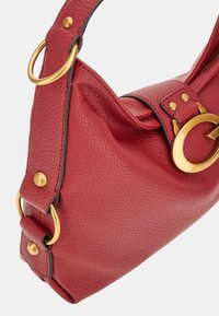 Borsa a spalla rossa in pelle con superficie testurizzata, hardware color oro e un grande accent circolare. Presenta un attacco laterale per la tracolla e una cerniera.