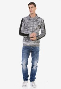 Grauer und schwarzer gestreifter Hoodie mit einem Kragen, strukturierten Ärmeln und einem Logo auf der Brust, kombiniert mit blauen Jeans und weißen Sneakern.