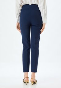 Marina byxor med hög midja, elegant design och avsmalnande ben. Tillverkade av ett slätt tyg med subtila sömnadsdetaljer.