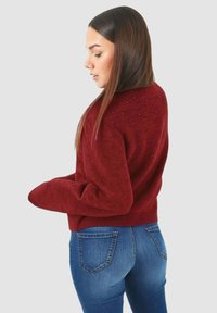 Maglione bordeaux in maglia con finitura strutturata e dettagli con perline sulle spalle, abbinato a jeans denim blu aderenti.