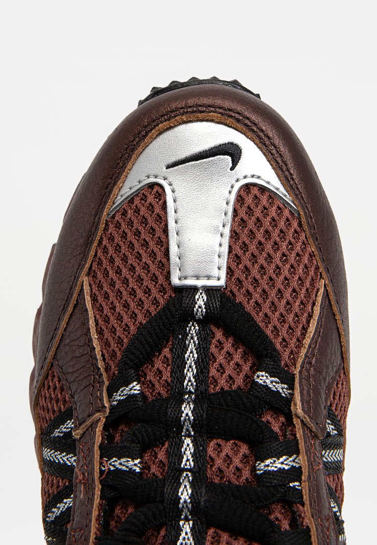Baskets Nike avec un dessus en maille marron, des accents en cuir, des détails argentés et des lacets noirs. Surface texturée et logo proéminent sur la languette.