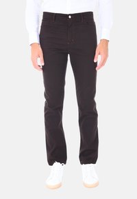 Pantaloni di cotone neri con vestibilità dritta, caratterizzati da dettagli di cucitura arancione, cinque tasche e chiusura con bottone. Indossati con sneakers bianche.
