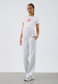 Umstandsmode bestehend aus einem weißen T-Shirt mit rosem Blumenmotiv und grauen Sweatpants mit einem breiten, elastischen Bund und seitlichen Taschen.