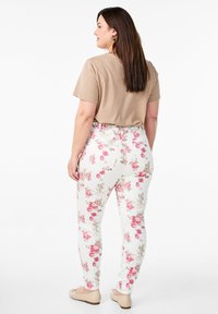 Pantalones florales de cintura alta en blanco con patrones de rosas en tonos rosa y beige, combinados con una camisa de manga corta beige y zapatillas crema.