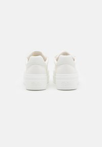 Pár bílých platformových tenisek s texturovanými podrážkami a logem "Buffalo" vyraženým na zadní straně, zobrazených zezadu na bílém pozadí.