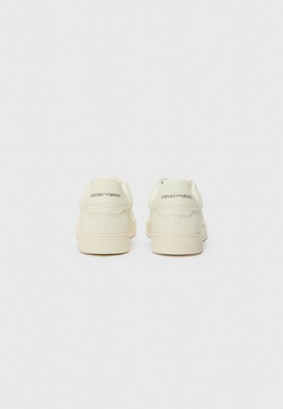 White leather sneakers with a smooth finish, featuring a tonal logo on the heel, and a textured rubber sole. Simple, minimalist design.