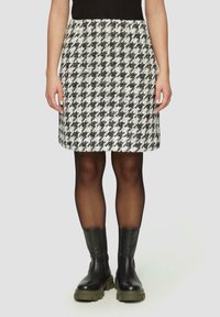 Falda pata de gallo en blanco y negro con cintura de tiro medio, confeccionada en tela texturizada. Combinada con botines negros hasta el tobillo y medias transparentes.