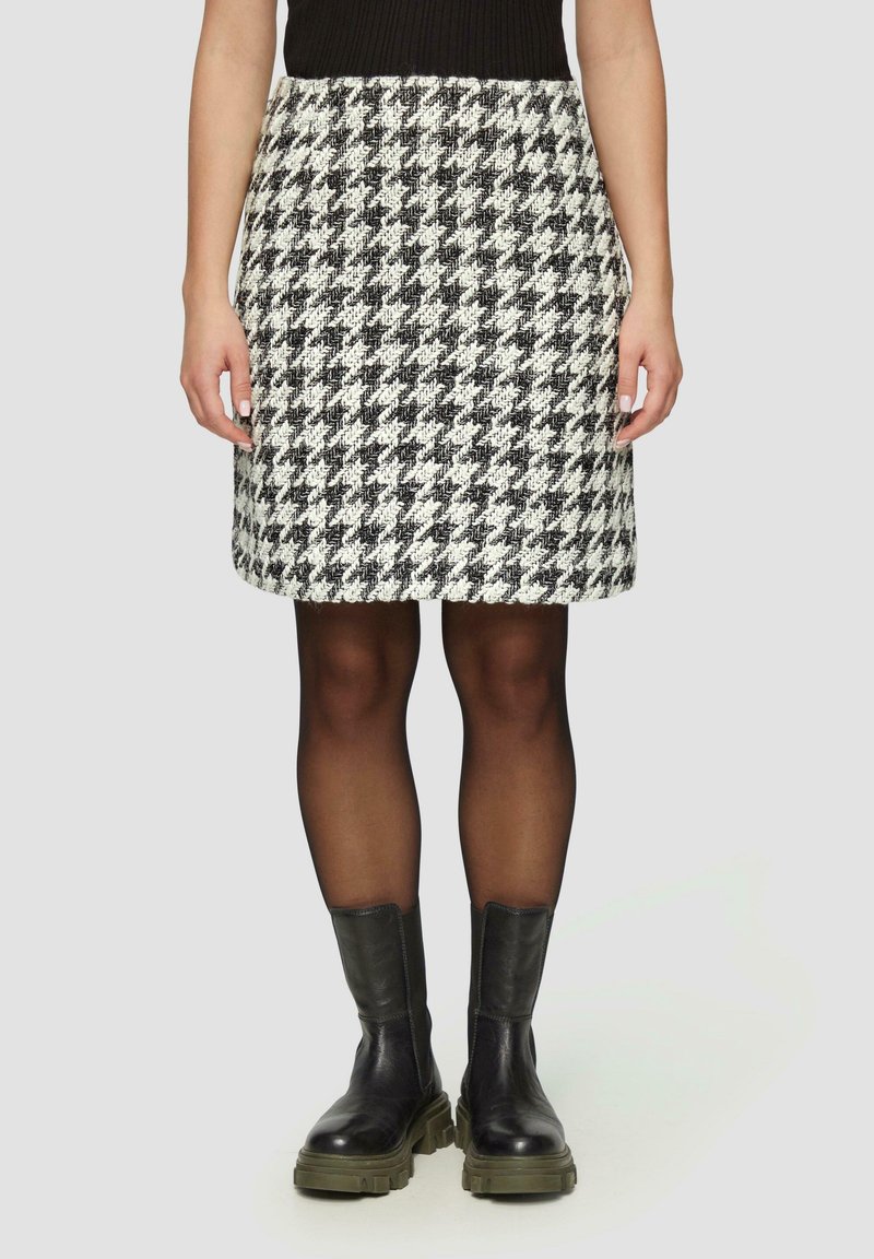 Falda pata de gallo en blanco y negro con cintura de tiro medio, confeccionada en tela texturizada. Combinada con botines negros hasta el tobillo y medias transparentes.