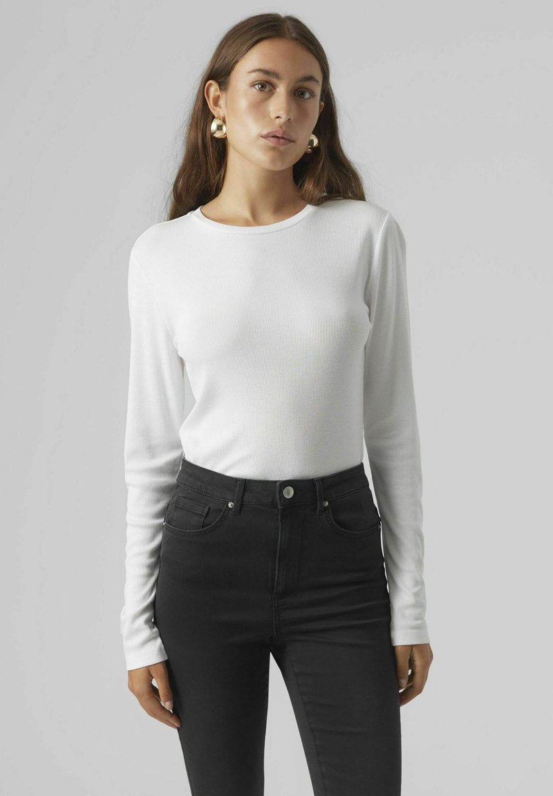 Weißes Langarm-Rippoberteil kombiniert mit schwarzen, hoch taillierten Jeans. Das Oberteil hat einen runden Ausschnitt und eine schmal geschnittene Passform und besteht aus einem weichen Material.