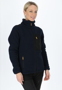 Navy fleece jacket with high collar, zipper pockets, black fabric accents, and textured material. Features a front zippered chest pocket.