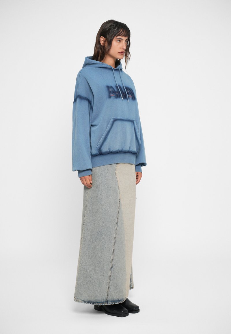 Lys blå hættetrøje med lomme foran og snore, parret med en lang denimnederdel med et splitdesign i to nuancer af blå.
