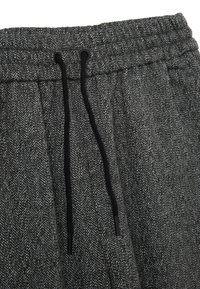 Pantaloni grigi a motivo a spina di pesce con cintura elastica e cordino nero. Tessuto testurizzato con sottili macchie bianche.