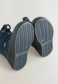 Blå støvler med en struktureret sort gummisål. Sålen har et fiskebensmønster for greb. Materialet fremstår holdbart med en polstret top.