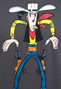 Grafisches T-Shirt mit einer Cartoon-Cowboy-Figur, die einen weißen Hut, ein gelbes Hemd, ein rotes Halstuch und blaue Jeans trägt. Grafische Kunst auf grauem Stoff.