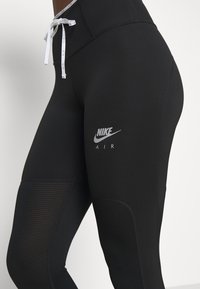 Czarne legginsy Nike o dopasowanym kroju, z siateczkowymi panelami po bokach i srebrnym logo w okolicy biodra. Elastyczny pas z białym sznurkiem.