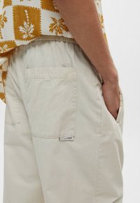 Pantalones beige con un acabado texturizado. Cuenta con un bolsillo trasero y una etiqueta cosida. Cintura elástica para mayor comodidad y un ajuste relajado.