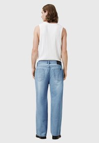 Svetlo modre široke jeans hlače z visokim pasom, z dvema zadnjima žepoma in črno etiketo na pasu. Nošene z belim brezrokavnikom.