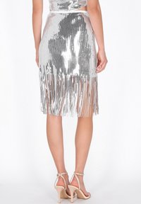 Ezüst flitteres rojtos szoknya, testhezálló derékkal, térd alá érő hosszúságban, hosszú rojttal a szegélyén. Bézs pántos magas sarkúval párosítva.