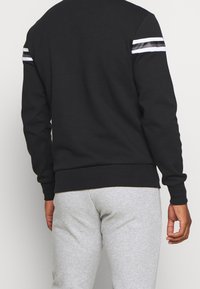 Sweat-shirt noir avec des rayures blanches et noires sur les épaules, poignets et ourlet côtelés, confectionné dans un matériau doux et texturé.