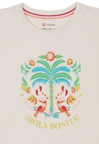 Jasno kremowa koszulka z kolorową palmą, kwiatami, owocami i dwoma ptakami w centralnym wzorze graficznym. Napis brzmi "¡HOLA BONITA!"