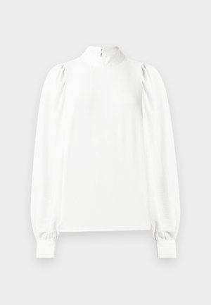 Blouse blanche à manches longues avec col montant, épaules bouffantes, poignets boutonnés et fermeture éclair dans le dos.