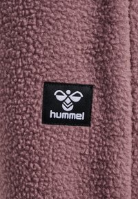 Fleece fabric in muted pink with a soft texture; features a black label with white logo and brand name "hummel" prominently displayed.