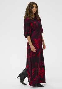 Maxi šaty v tmavě fialové barvě s červenými květinovými vzory, krátkými nabíranými rukávy a detailem staženého pasu. V kombinaci s elegantními černými kotníkovými botami.