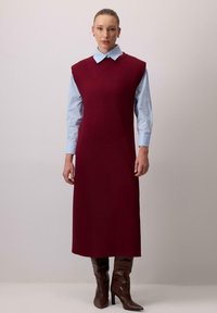 Burgundi värvi ilma varrukateta kleit kõrge kaelusega, mille peal on helesinine kaelusega särk. Pruunid põlvikud lõpetavad välimuse.