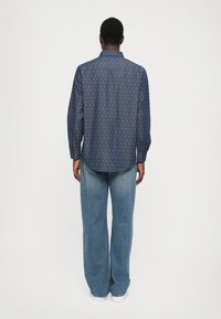 Camisa de botón azul marino con un sutil patrón de lunares, de manga larga y con un cuello clásico, combinada con jeans de pierna ancha en azul claro.