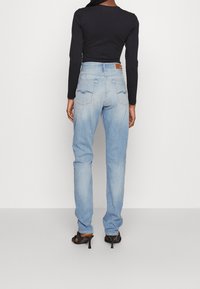 Ljusblå denimjeans med rak passform, fem fickor och dekorativ sömnad på bakfickorna. Bärs med en svart långärmad topp.