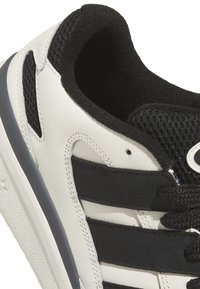 Sneaker bianco in pelle con accenti in rete nera, strisce nere e lacci neri. Suola testurizzata con dettaglio del logo sul lato.