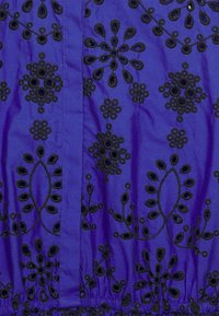 Tissu bleu avec broderie florale noire présentant des formes circulaires et ovales dans un motif répété.