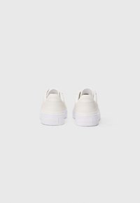 White leather sneakers with a smooth surface, rounded shape, and a raised white sole. Branding embossed on the heel.
