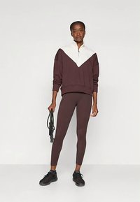 Bordowa bluza z białymi blokami kolorystycznymi i zamkiem przy szyi, zestawiona z pasującymi legginsami z wysokim stanem, noszona z czarnymi trampkami.