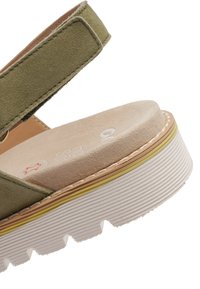 Zelená semišová sandála s mäkkou béžovou stielkou. Hrubá biela platformová podrážka má textúrovaný povrch a žltú akcentovú linku. Nastaviteľný remienok.