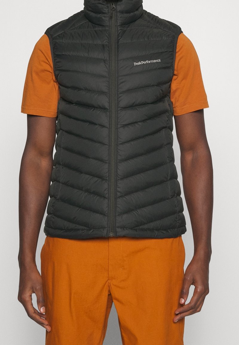 Czarna, puszysta kamizelka z zapięciem na zamek błyskawiczny i stebnowanym wzorem w chevrony. Bezrękawnik z wysokim kołnierzem. Noszona na pomarańczowej koszuli.