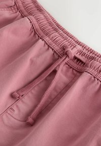 Ceinture élastique sur un pantalon rose poudré avec cordon de serrage et détail de couture sur la poche avant.