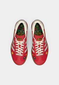 Červené tenisky s bílými pruhy a květinovou výšivkou. Pryžová podrážka, texturovaná tkanina a kontrastní vnitřní podšívka s barevným květinovým vzorem.